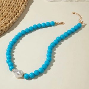 Détail d'un collier de perles bleu vif avec une grande perle baroque et un fermoir doré