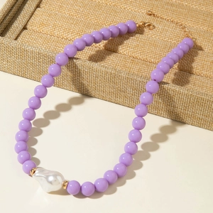 Détail de perles violettes avec un pendentif perle baroque sur chaîne dorée réglable