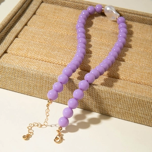 Détail du collier de perles violettes avec une perle baroque blanche et fermoir doré