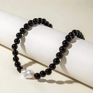 Détail d'un bracelet en perles d'onyx noir et une perle baroque sur un socle blanc pur