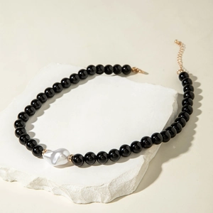Collier minimaliste en perles noires avec une grande perle baroque sur une dalle en pierre