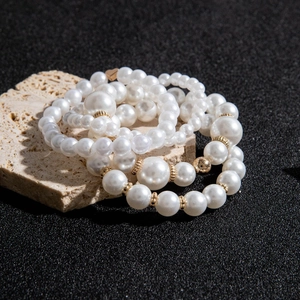 Detail of multi-layer faux pearl bracelet set with gold metal spacers on dark sand