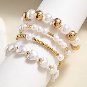 Detail of four-piece gold beaded and heart pearl bracelet set on a white display stand