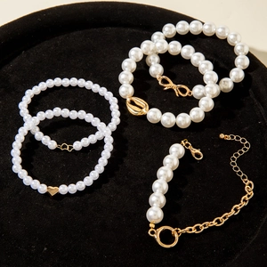 Close-up of five pearl bracelets with gold heart and shell charms on black velvet