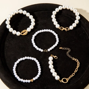 Detail of 5-piece pearl bracelet set with gold heart and shell charms on black velvet tray