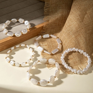 Detailed close-up of 5-piece white pearl bracelet set with gold beads on velvet tray