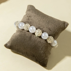 Macro view of white pearls and sparkling rhinestone balls on a brown velvet cushion