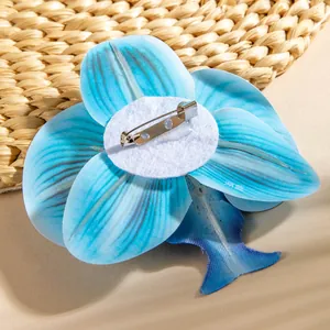 Detail of lake blue orchid brooch back with silver safety pin and felt pad on straw mat