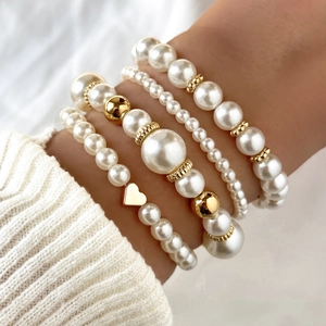 Elegant 4-piece layered pearl bracelet set with a gold heart pendant on a woman's wrist