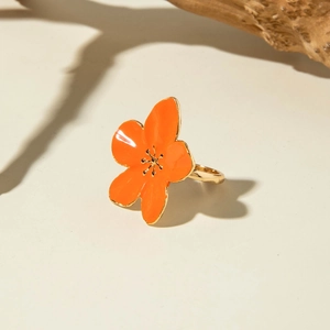 Detail of vibrant orange enamel flower ring with golden filaments on minimalist background