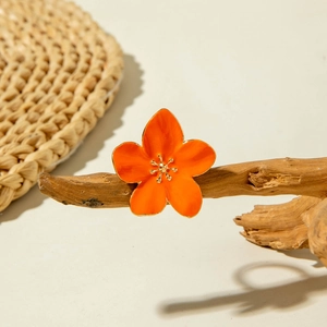 Macro detail of orange enamel flower ring with golden metallic center on wood branch