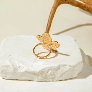 Detailed view of gold flower ring with hammered metal texture on a stone pedestal