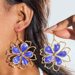 Close-up of oversized hollow flower earrings with purple glitter enamel and gold trim
