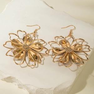 Detailed view of gold flower earrings with layered hollow petals on white stone
