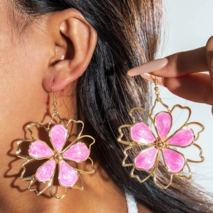 Detailed view of large gold-tone flower earrings with pink enamel inlay on a model