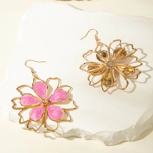 Detailed close-up of gold-plated flower earrings with pink enamel inlay on white stone