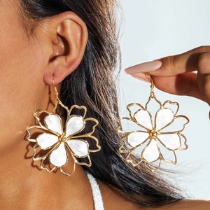 Close-up of oversized gold-plated flower earrings with white enamel petals on a blue background
