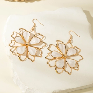 Detailed macro view of large gold-rimmed white enamel flower earrings on a stone base