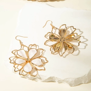 Detailed view of asymmetric gold floral earrings with white enamel on a stone surface