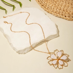 Detail of a large gold floral pendant necklace with white enamel petals on a stone slab