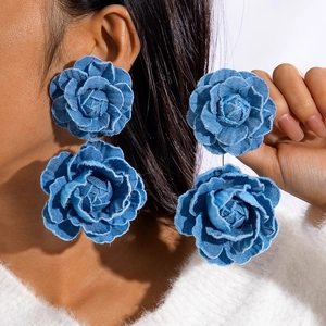Detailed close-up of large blue denim rose floral drop earrings worn by a model