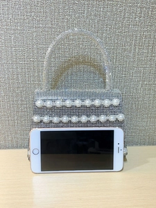 Mini silver evening bag with rhinestones and pearls shown next to a smartphone for size scale