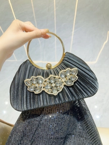 Detail of black pleated evening clutch with crystal flower and gold metal ring handle