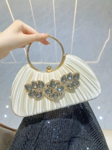 Detail of cream pleated satin evening clutch with emerald gemstone and gold ring handle