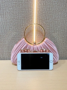 Detail of pink pleated evening clutch with golden ring handle and rhinestone accents