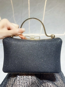 Close-up of black sparkly clutch bag featuring golden bow clasp and round metal handle