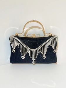 Close-up of black evening clutch with rhinestone tassels and golden bow clasp