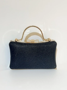Detail of black glitter evening clutch featuring a gold metal handle and rhinestone bow clasp