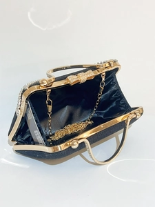 Detail of black evening clutch bag with crystal bow clasp and gold chain strap inside