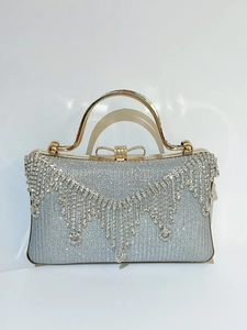 Detail of silver evening clutch bag featuring rhinestone tassels and a gold bow clasp