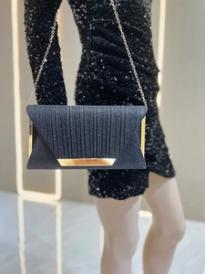 Detail of elegant black pleated evening clutch with gold metal trim and chain strap