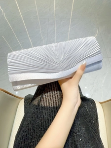 Pochette de soirée plissée argentée tenue sur une robe à paillettes pour l'élégance