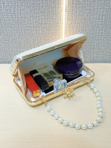 Detail of white pleated evening clutch with pearl handle showing interior storage capacity