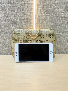 Golden rhinestone evening clutch bag with metal handle compared to a smartphone for size