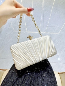 Detail of pleated cream evening bag with pearl handle and golden cross-shaped clasp