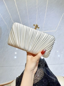 Detailed view of cream pleated satin clutch featuring a gold metal knot clasp for events