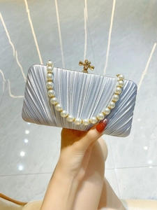 Detail of silver pleated evening clutch bag with pearl handle and golden knot clasp