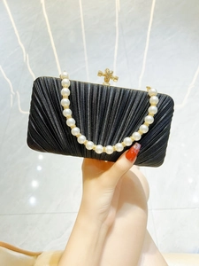 Detail of black pleated evening bag featuring a white pearl handle and gold knot clasp