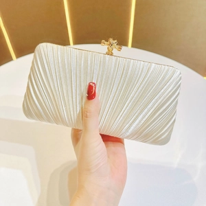 Close-up of white pleated evening clutch featuring a luxury gold knot clasp decoration