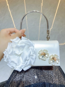 Close-up of white satin evening bag featuring delicate fabric flowers and pearl accents