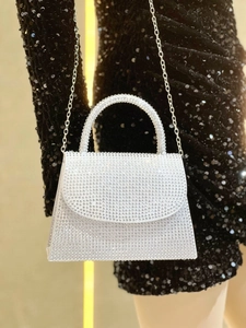 Detail of silver rhinestone evening bag with chain strap and glossy handle on black dress