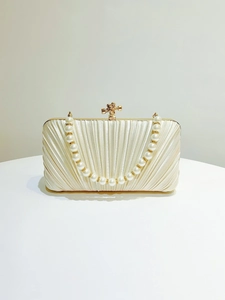 Detail of pleated satin evening bag with pearl chain handle and golden bow clasp