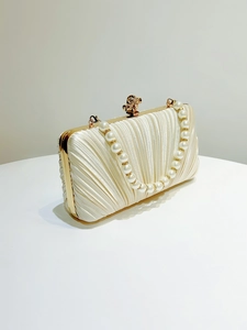 Detail of cream silk pleated evening bag with elegant pearl handle and gold metal clasp