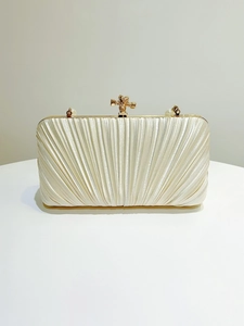 Detail of champagne pleated evening clutch with golden knot clasp and pearl accents