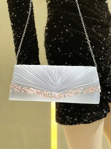 Détail d'une pochette de soirée argentée plissée avec strass sur une robe noire