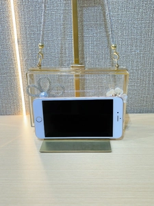 Macro detail of acrylic clutch bag showing rhinestone bow and interior phone capacity